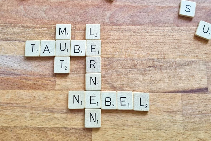 Spieltsteine eines Buchstaben-Legespiels liegen auf einem Tisch und bilden verchiedene Wörter